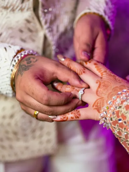 Another angle of the ring exchange, this time focusing on the groom placing the ring on the bride's finger, with her intricate henna on display.
