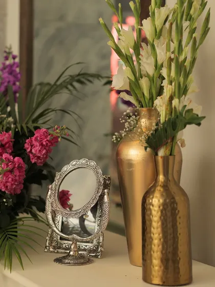 A close-up of a decor vignette, showing how we mix textures and finishes. A hammered gold vase, a smooth silver mirror, and fresh flowers create a balanced and elegant composition.
