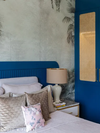 This bedroom features a bold royal blue color for the wardrobe and headboard. A tropical, monochromatic wallpaper behind the bed adds a sense of depth and creates a stunning feature wall.