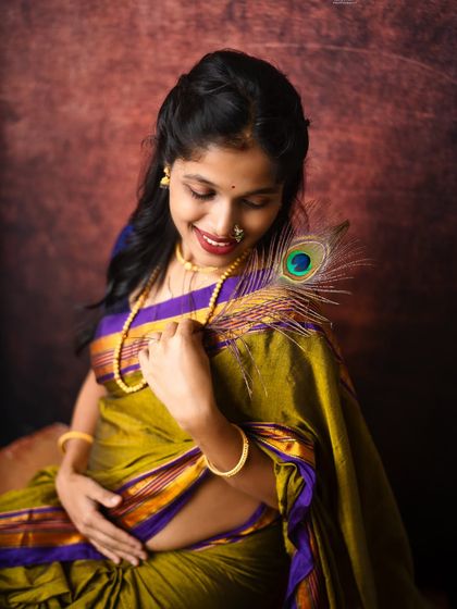 A close-up portrait highlighting the beauty of traditional details, from the nose ring and gold jewelry to the peacock feather gently brushing her shoulder.