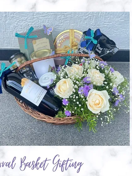 A luxurious floral basket for a housewarming gift. This beautiful arrangement includes a bottle of non-alcoholic wine, snacks, and fresh white roses in a rustic wicker basket.