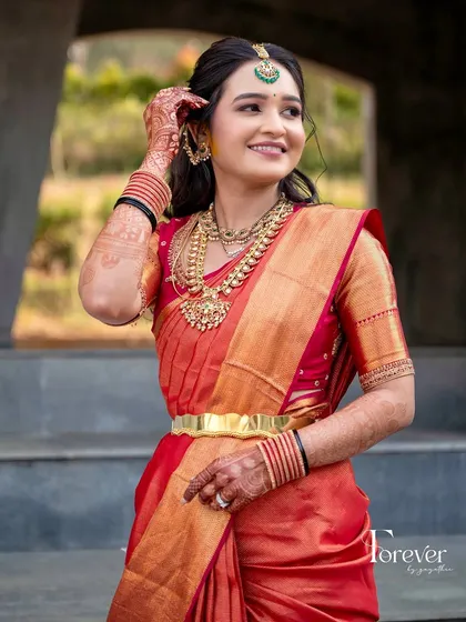 A full-length shot of a bride in her red and gold Kanchipuram saree. The custom blouse and traditional gold jewelry create a perfect bridal look for her Varapooja.