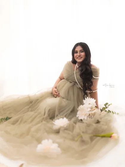 A joyful, relaxed portrait of the mother-to-be seated amongst scattered flowers. Her bright smile and the playful setup create a light and happy mood.