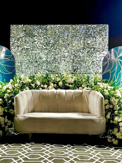Modern, chic, and glamorous. This reception stage combines a shimmering sequin backdrop with artistic teal panels and an abundance of white flowers, creating a contemporary and high-fashion look.