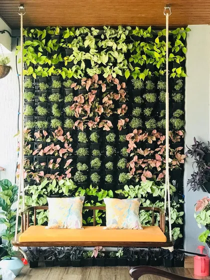 A closer view of the completed balcony garden. You can see the detail in the plant selection, with pink and light green foliage creating a soft pattern against the dark green base, perfectly framing the swing.