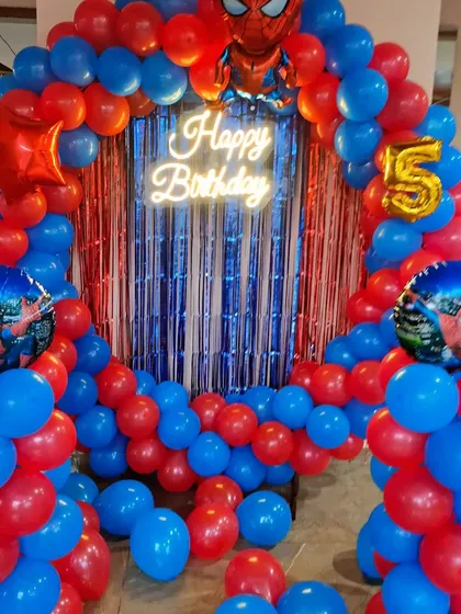 A Spiderman theme with a circular balloon arch in red and blue. A neon sign and foil Spiderman balloons complete the superhero look.