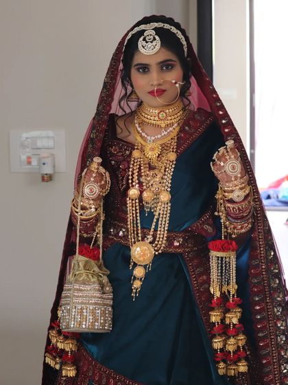 All set for the Nikaah ceremony. This traditional Muslim bridal look features heavy gold jewellery, a beautiful teal and maroon outfit, and makeup that highlights her eyes.