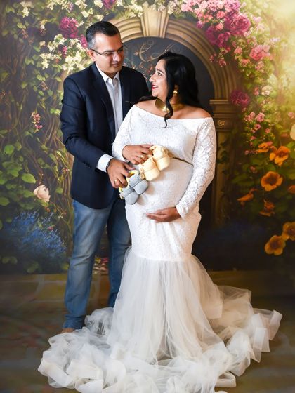 A sweet couple's portrait in our studio, holding two pairs of baby shoes to announce their twins.