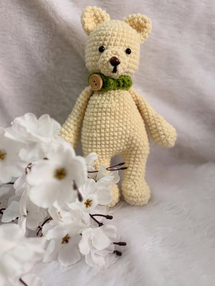 A classic teddy bear design with a green collar and a wooden button detail.