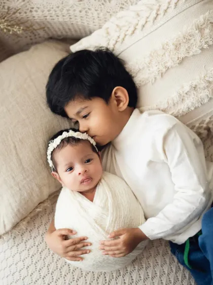 A gentle kiss on the forehead from a big brother to his baby sister. These newborn and toddler poses are perfect for capturing sibling love.