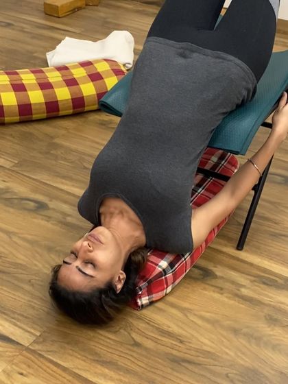 A close-up of a student in a supported backbend over a chair. The expression of peace on her face shows the deep relaxation this pose brings.