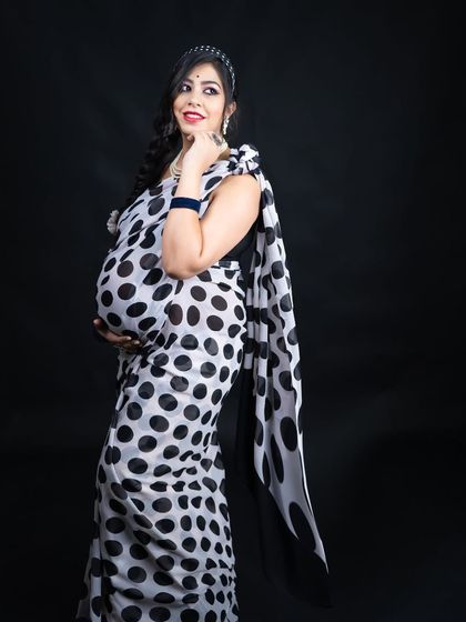 A fun and fashionable take on the saree maternity shoot. The mom-to-be poses confidently in a black and white polka dot saree, showing off her baby bump with style.