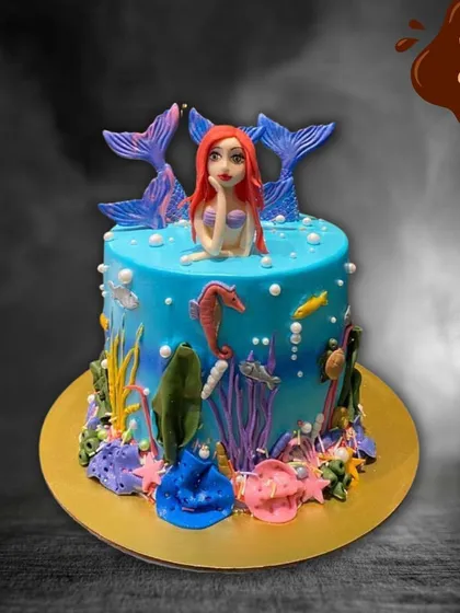 A vibrant blue mermaid cake that captures the beauty of the ocean. The design is rich with colorful fondant coral, seaweed, a seahorse, and a graceful mermaid figure.