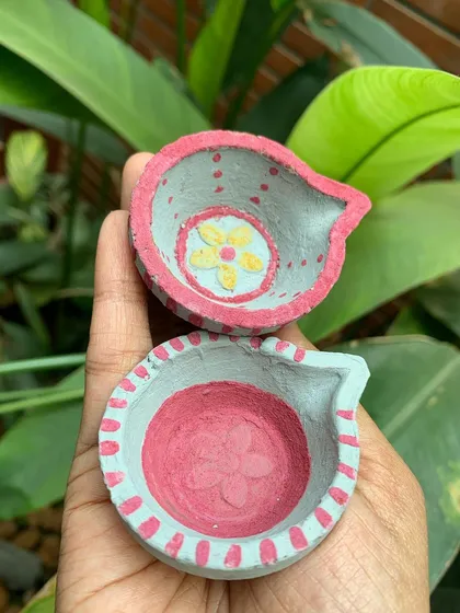 A pair of finished diyas, ready to be lit. The combination of the earthy terracotta and the soft, natural paint colours creates a warm and inviting feel.