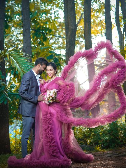 A romantic portrait of a couple in a forest setting. The dramatic, heart-shaped swirl of the gown's train adds a magical, artistic element to this nature-filled shot.