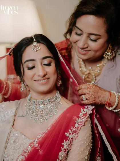 A mother helps her daughter, the bride, adjust her red veil. This gentle, caring moment during the getting-ready process is a timeless part of the wedding story.