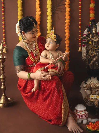 A serene portrait of a mother and child looking at each other, surrounded by traditional Janmashtami decorations.
