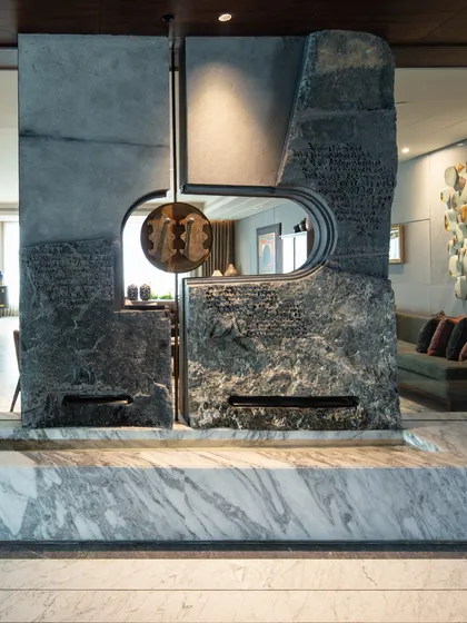At the entrance of The 42 residence in Kolkata, we designed this majestic water feature to be the home's focal point. Crafted from massive, naturally textured stone slabs, it is adorned with brass and silver ‘Khadau’ (traditional Indian footwear) and etched Pali script, symbolizing blessings and a serene welcome. The sound and sight of water create a tranquil threshold.