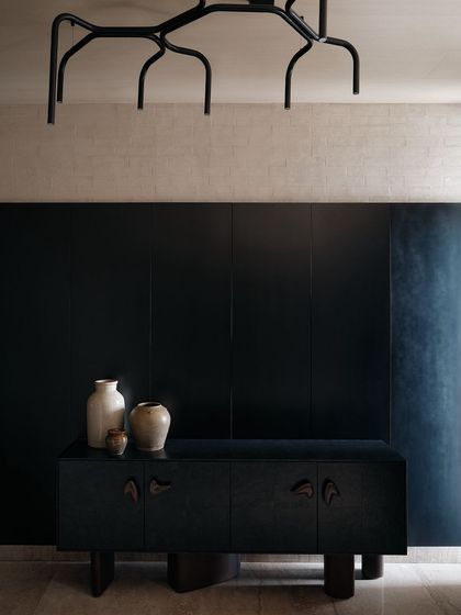 The foyer console is a minimalist piece with unique, hand-carved handles. Paired with a modern chandelier and simple ceramic vases, it creates an elegant and welcoming first impression.