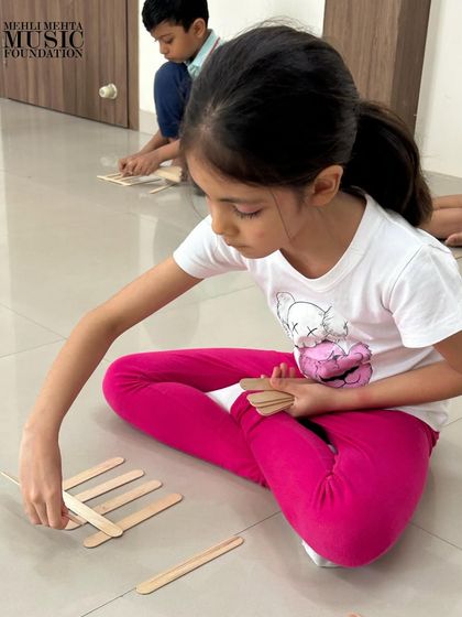 A student practices notating rhythm patterns with popsicle sticks. This tactile method helps solidify the understanding of musical notation in a playful, engaging manner.
