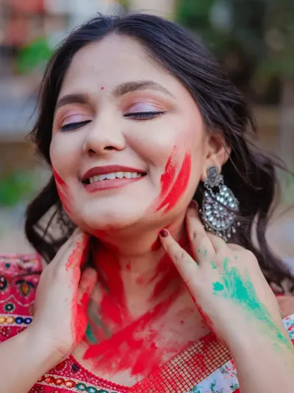 A close-up from an outdoor Holi shoot. The model's joyful expression and the smear of red and green colors create a warm and festive portrait.
