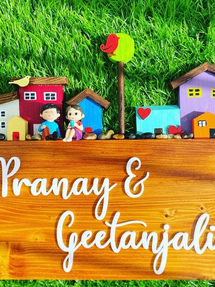 This custom nameplate features a row of colorful miniature houses, each with its own unique character. The 3D acrylic names stand out beautifully against the warm, stained solid wood base, creating a cheerful and welcoming entrance sign.