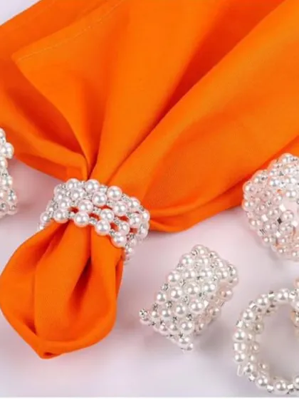 Timeless elegance is all in the details. These white pearl napkin rings add a touch of classic sophistication to any dining experience, shown here beautifully complementing a vibrant orange napkin for a modern twist.