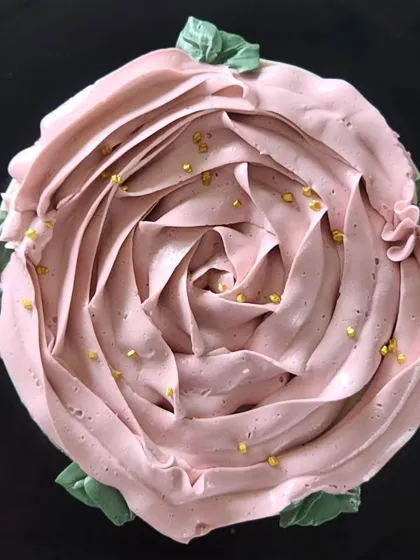 A top-down view of a beautiful vanilla and strawberry cake. I used a soft pink vanilla buttercream to pipe this large rose design, adding a few hand-piped leaves and a sprinkle of gold dust for a floral, elegant finish.