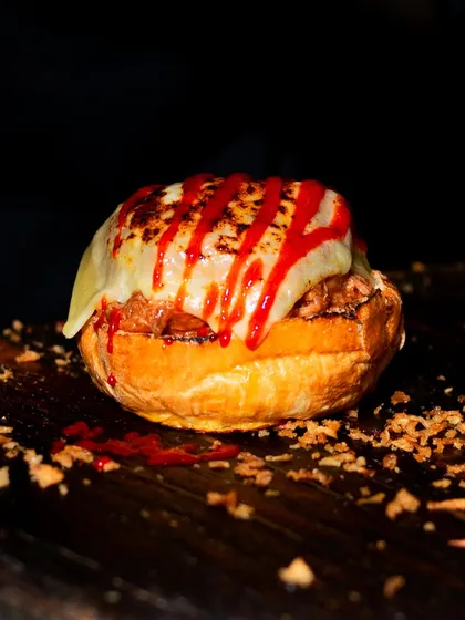 A close-up of a saucy, cheesy pulled pork bagel. The focus is on the messy, delicious toppings that make the dish so appealing.