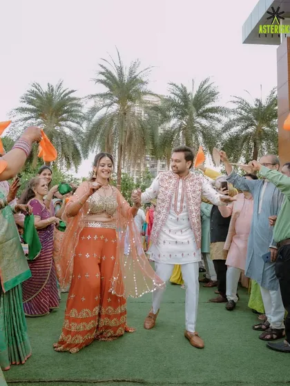 The couple's grand entry at their Haldi, dancing through a tunnel of guests waving orange flags.