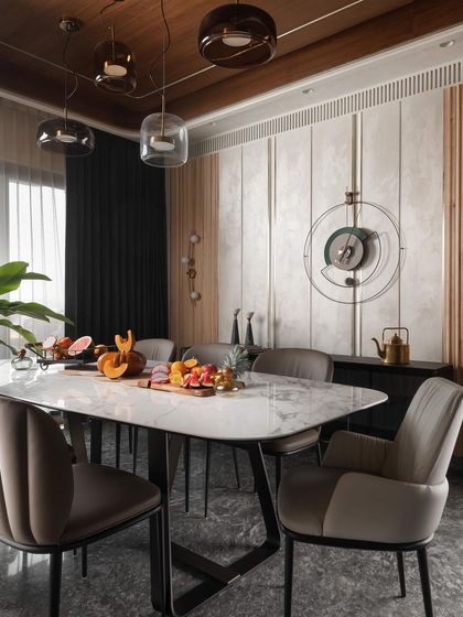 The dining area is defined by a curved ceiling detail and a sophisticated mix of materials. A marble-topped table is surrounded by comfortable upholstered chairs, set against a backdrop of textured wall panels and wood fluting.