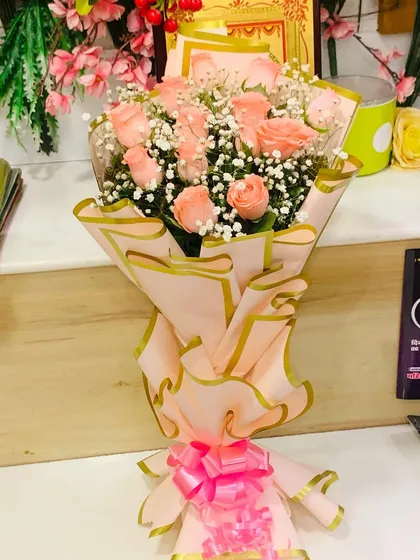 A lovely bouquet of peach roses and baby's breath. The soft pink wrapping paper has a gold trim, adding a touch of elegance to this sweet arrangement.