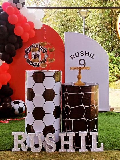 A dynamic football-themed ninth birthday party. The outdoor setup includes a Manchester United crest, football-print plinths, and a large light-up number '9'.