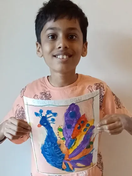 The proud smile of an artist with his finished masterpiece says it all. This student is showing off his vibrant peacock painting, a beautiful result of learning color blending and brush techniques in our acrylics class.