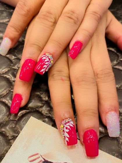 A bold and beautiful set of bright pink square nails. The design includes white glitter accent nails and pink nails with hand-painted white floral art and crystal centers.