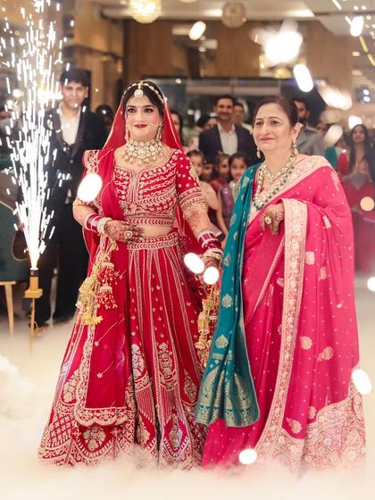 The bride's grand entrance with her mother. The sparklers highlight her glowing makeup and stunning red bridal attire.