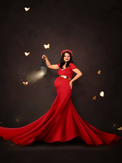A striking solo portrait in a vibrant red gown. The mom-to-be holds a lantern with sparkling effects, creating a magical and captivating image against a dark background.