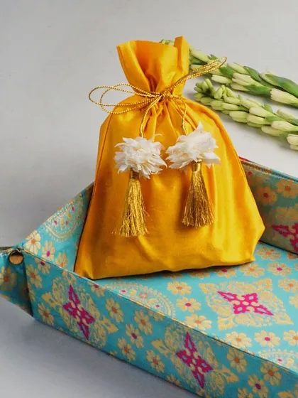 A clean and simple composition focusing on a yellow potli bag. The addition of fresh tuberoses adds a touch of elegance and a hint of fragrance to the visual story.