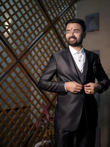 A dapper portrait of the groom. Dressed in a sharp black suit, he looks happy and ready for the big day, captured in a moment of candid confidence.