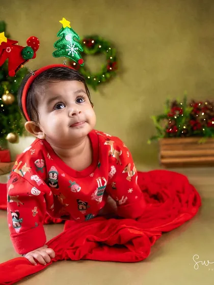 Dressed in a festive red sweater, this baby is enjoying her first Christmas photoshoot.