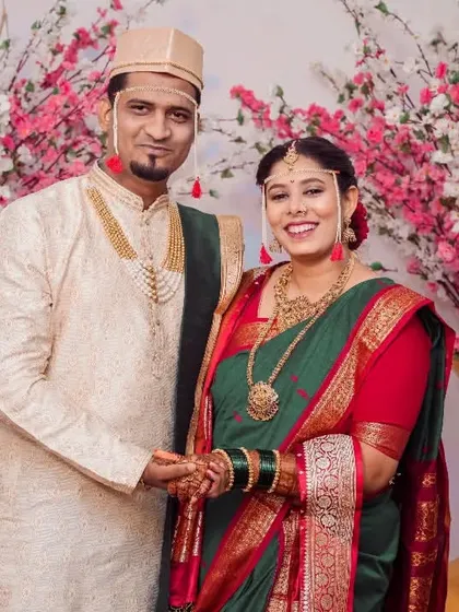 A lovely portrait of a couple in traditional green and red Maharashtrian wedding attire, standing before a floral backdrop.