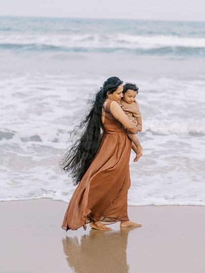 A mother and child walking on the beach. The flowing dress and the ocean waves create a beautiful, poetic image.