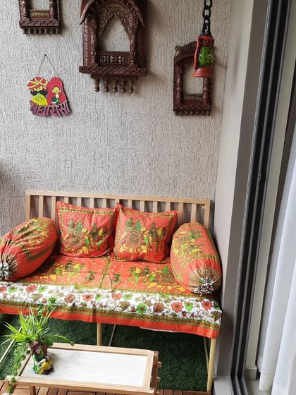 Here is another view of the Rajasthani-themed balcony. The combination of the pinewood bench, traditional textiles, and ethnic wall decor like the jharokhas and puppets creates a truly unique and culturally rich seating area.