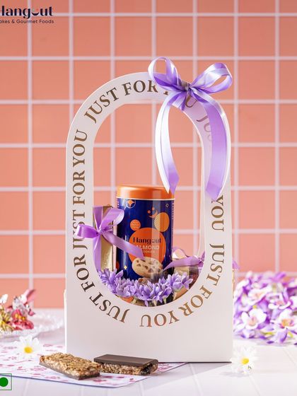 The Indulgence Hamper is a luxurious gift for Women's Day. It includes handmade almond cookies, gluten-free bliss bars, and chocolate barks, all presented in a reusable 'Just For You' gift basket.