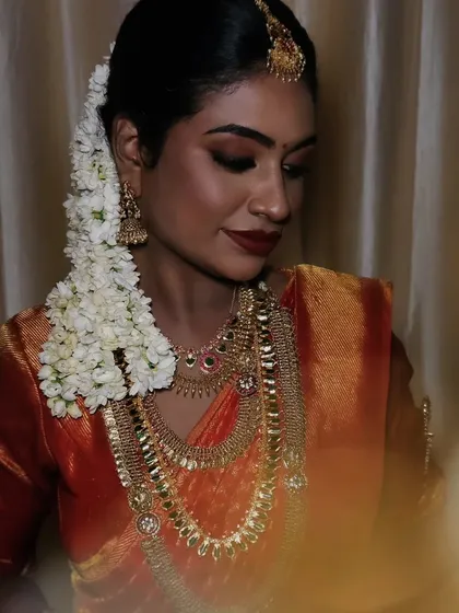 A close-up of a dusky bride, looking down gracefully. The makeup enhances her features beautifully, and the traditional jewelry adds to the regal look.