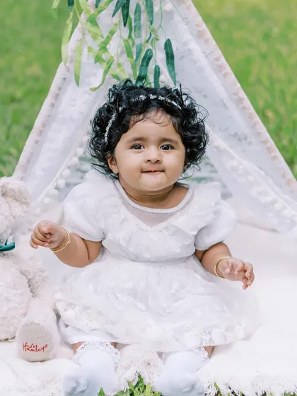 A beautiful portrait of the birthday girl in her white dress, sitting in a teepee outdoors.
