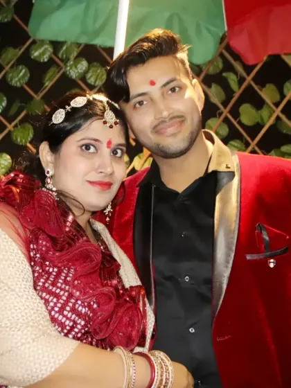 A couple dressed in festive red outfits poses for a photo at an evening event.