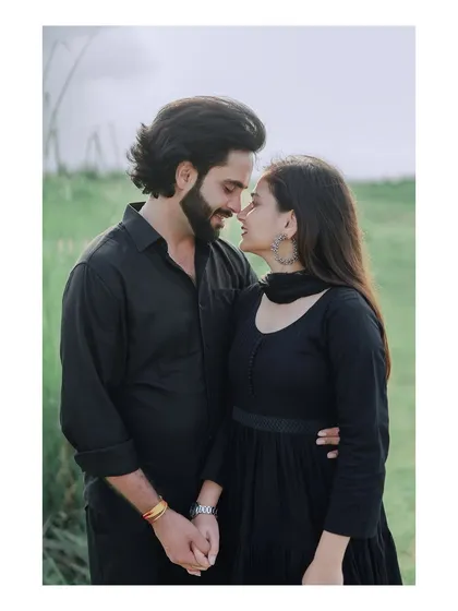 An intimate portrait of a couple in matching black outfits, their connection shining through in a natural, green setting.
