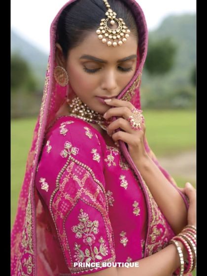 A beautiful close-up of the handcrafted pink bridal lehenga, showing the delicate embroidery on the blouse sleeve and the traditional maang tikka.