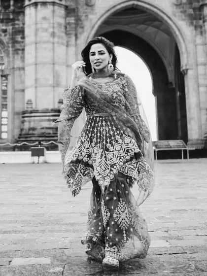 A full-length black and white shot capturing the bride's graceful movement. The historic archway in the background adds a sense of grandeur.